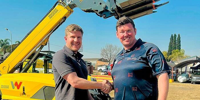 Men shaking hands in front of a Wacker Neuson telehandler