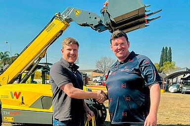 Men shaking hands in front of a Wacker Neuson telehandler