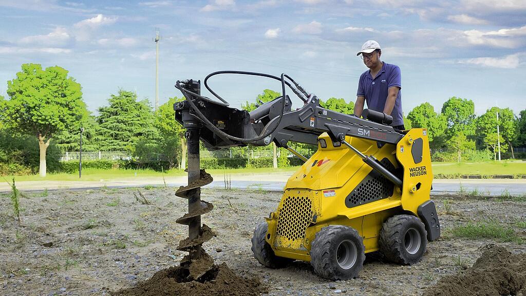 Mini loader on wheels with auger in action