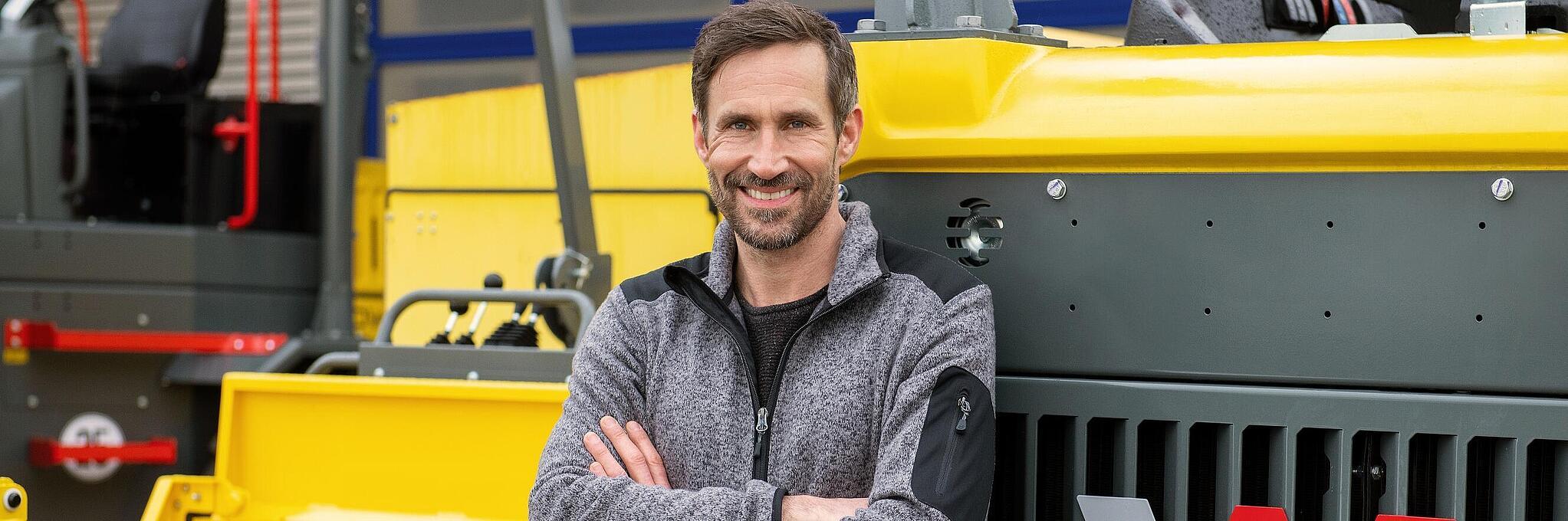 Smiling Wacker Neuson employee, arms crossed, leaning against a Wacker Neuson construction machine.