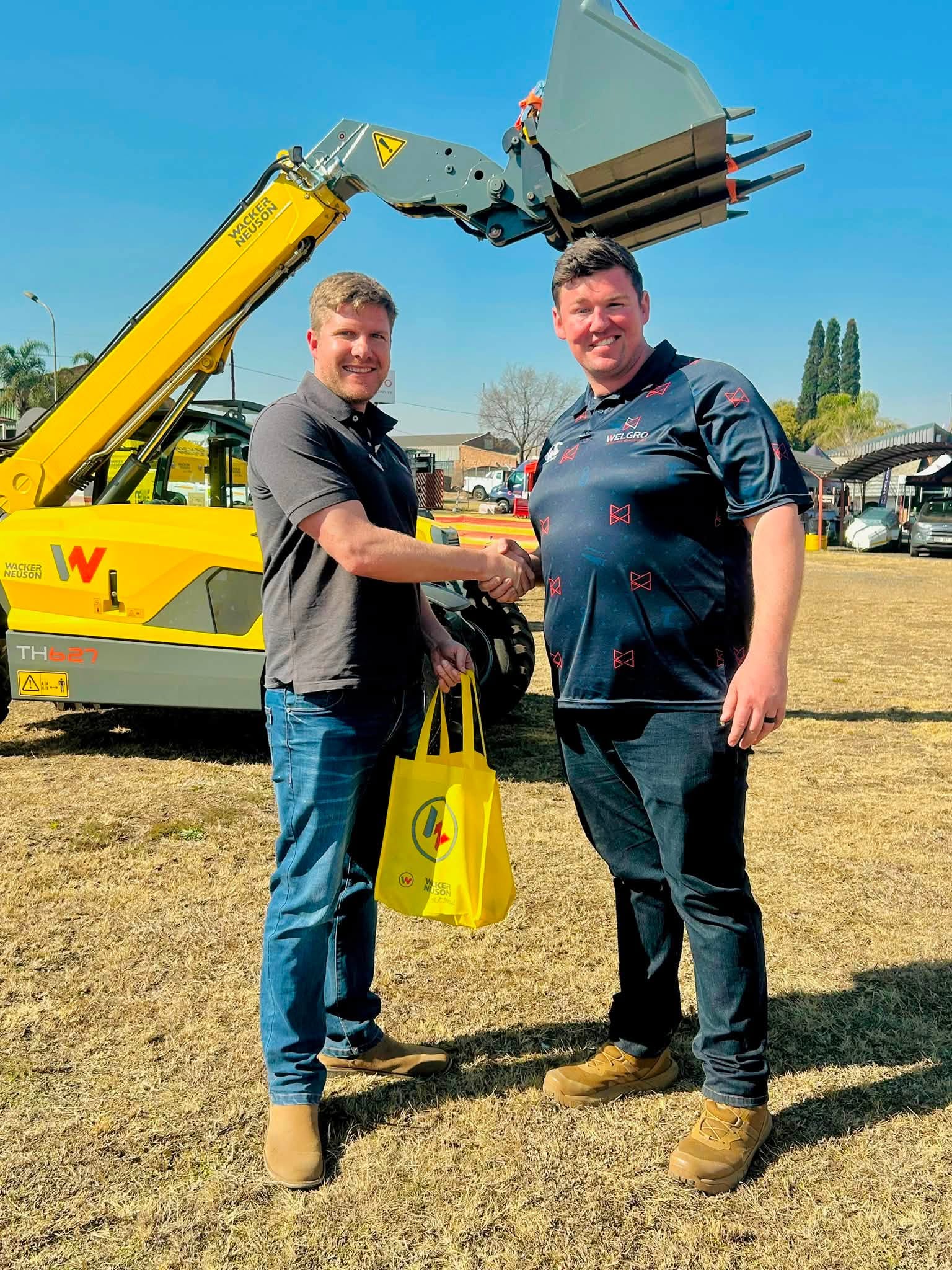 Men shaking hands in front of a Wacker Neuson telehandler